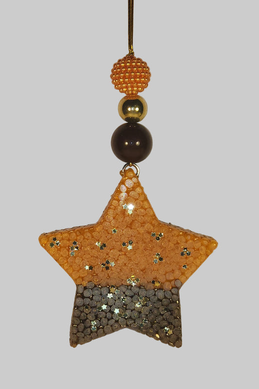A decorative star-shaped accessory with a glittery orange and dark brown split design, attached to a thin elastic string with three beads (orange textured, gold, and dark brown) on a plain light background.